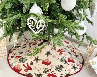May include: A decorated Christmas tree with white ornaments and a festive tree skirt. The tree skirt features a cream background with red gift boxes, bows, candy canes, and holly. The skirt has a red border.