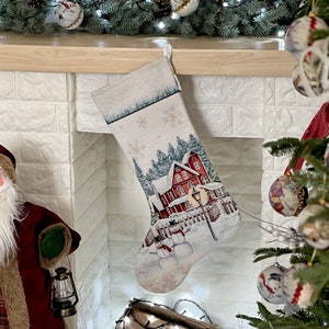 May include: A white Christmas stocking with a red and white house and snowmen design. The stocking is hanging on a white brick fireplace mantel.
