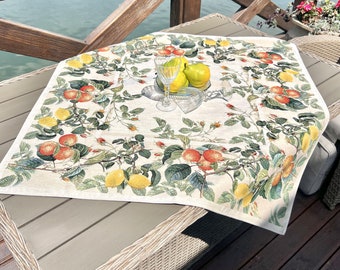 May include: A white tablecloth with a lemon and orange floral pattern. The tablecloth is laid on a wooden table with a wicker chair in the background.