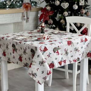 Puede incluir: Un mantel blanco con un patrón de gnomo navideño. El mantel está puesto sobre una mesa blanca con una silla blanca. El mantel tiene un patrón rojo y verde con pequeños puntos blancos.
