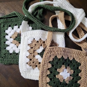 May include: Four crochet tote bags in shades of green, white, and brown. Each bag features a square granny stitch design with coordinating straps. The bags are handmade and appear to be made of cotton yarn.