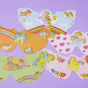May include: Six colorful paper My Little Pony party favor masks. Each mask features a different pony with a rainbow, hearts, or flowers. The masks are perfect for a My Little Pony themed party.