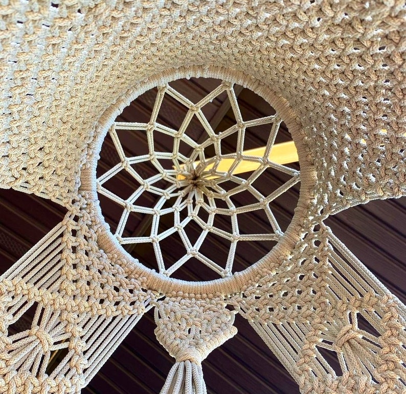 May include: A white macrame wall hanging with a circular design in the center. The macrame is made of thick cotton cord and has a fringe at the bottom.