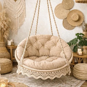 May include: A beige, tufted, round hanging chair with a macrame trim. The chair hangs from thick, twisted rope. The room has a bohemian theme with woven decor, a patterned rug, and natural light.