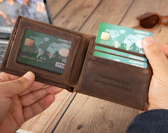May include: A brown leather bifold wallet featuring a clear ID window slot, multiple card slots, and an interior engraving that reads, Forever my love, always in my heart. The wallet contains green credit cards with a world map graphic design.