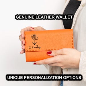 May include: An orange genuine leather wallet with a floral design and the name "Cindy" in script. The wallet is held by a person. The text "GENUINE LEATHER WALLET" and "UNIQUE PERSONALIZATION OPTIONS" are displayed.
