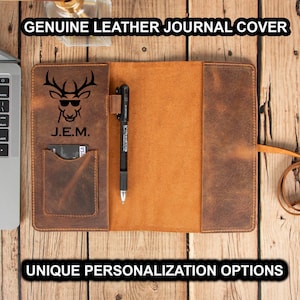May include: A brown leather journal cover featuring a deer silhouette and the initials "J.E.M." embossed on the front. The cover includes a pen loop and a pocket for cards or other small items.