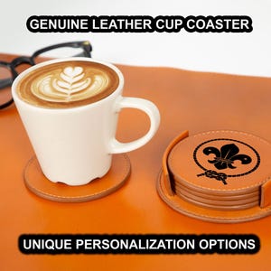 May include: Genuine leather cup coasters in a stack and individually. The coasters are brown with a decorative black design. A white coffee cup with latte art sits on a coaster. Text reads "GENUINE LEATHER CUP COASTER" and "UNIQUE PERSONALIZATION OPTIONS."