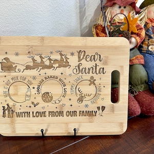 May include: A wooden cutting board with an engraved design of Santa Claus in a sleigh pulled by reindeer. The board also has a message that says "Dear Santa" and "With love from our family".