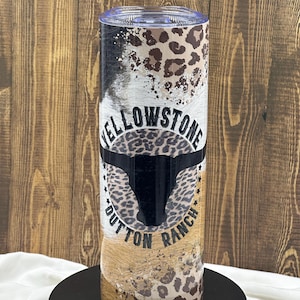 May include: A stainless steel tumbler with a "Yellowstone Dutton Ranch" design. The tumbler features a mix of animal print patterns, including leopard spots and cowhide textures, with the ranch logo prominently displayed.