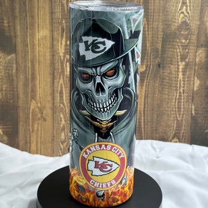 May include: A stainless steel tumbler featuring a skull wearing a Kansas City Chiefs hat and a red, white and yellow logo that reads "Kansas City Chiefs".