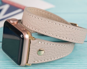 May include: A light gray leather Apple Watch band with a rose gold watch face. The band is double-wrapped around the watch.