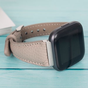 Op de afbeelding: Een grijs leren horlogebandje met een zwart vierkant smartwatch-scherm.