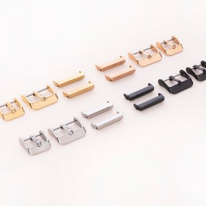 K&ouml;nnte beinhalten: Ein Satz von 10 Uhrenarmband-Schlie&szlig;en in drei verschiedenen Ausf&uuml;hrungen: Gold, Ros&eacute;gold und Schwarz. Die Schlie&szlig;en sind in Reihen auf einer wei&szlig;en Oberfl&auml;che angeordnet.