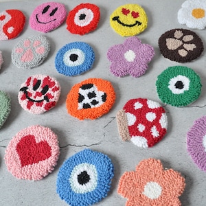 May include: A collection of colorful, round, hand-stitched felt coasters with various designs, including smiley faces, flowers, eyes, and hearts.