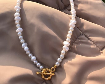 May include: A white pearl necklace with a gold toggle clasp. The necklace is made of irregular shaped pearls.