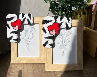 May include: Two wooden picture frames with white mounts and black and white patterned fabric hearts with red and pink accents. The frames are on a wooden surface.