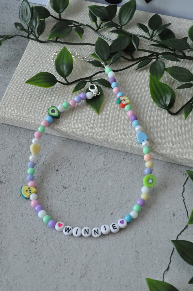 May include: A colorful beaded necklace with fruit charms and the name "WINNIE" spelled out in white beads with pink hearts.