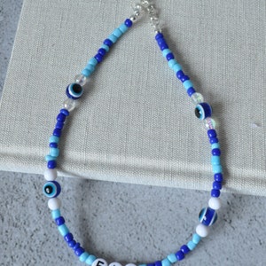 May include: Blue and white beaded necklace with evil eye charms and the name "ELI" spelled out in white beads.