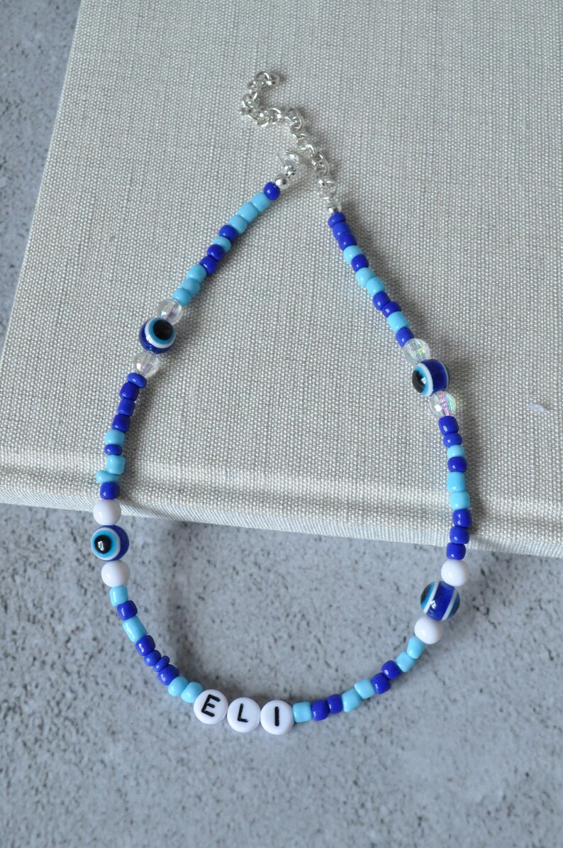 May include: Blue and white beaded necklace with evil eye charms and the name "ELI" spelled out in white beads.