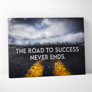 K&ouml;nnte beinhalten: Leinwanddruck mit einer Stra&szlig;e mit gelben Linien unter einem bew&ouml;lkten Himmel. Der wei&szlig;e Text lautet "THE ROAD TO SUCCESS NEVER ENDS". Geeignet f&uuml;r die Inneneinrichtung.