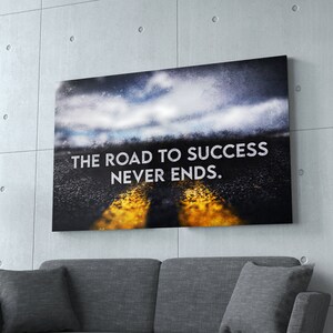 K&ouml;nnte beinhalten: Leinwanddruck mit dem Text "THE ROAD TO SUCCESS NEVER ENDS". Das Bild zeigt eine Stra&szlig;e mit gelben Linien, die zu einem bew&ouml;lkten Himmel f&uuml;hrt. Das Kunstwerk wird &uuml;ber einem grauen Sofa vor einer Betonwand ausgestellt.