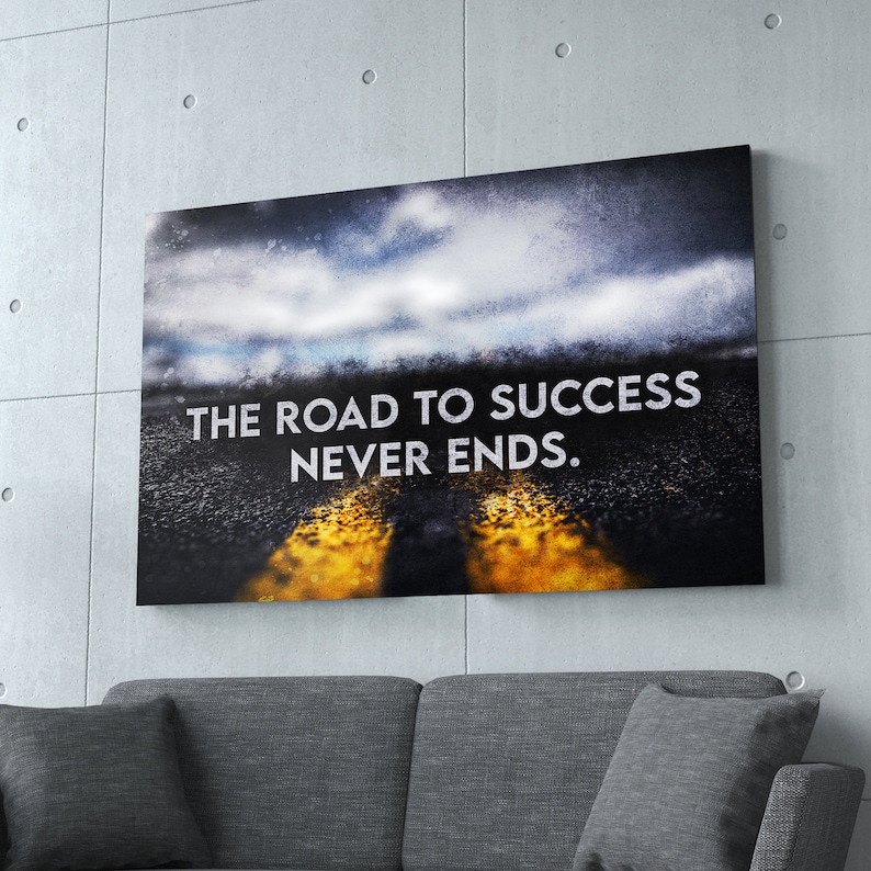 K&ouml;nnte beinhalten: Leinwanddruck mit dem Text "THE ROAD TO SUCCESS NEVER ENDS". Das Bild zeigt eine Stra&szlig;e mit gelben Linien, die zu einem bew&ouml;lkten Himmel f&uuml;hrt. Das Kunstwerk wird &uuml;ber einem grauen Sofa vor einer Betonwand ausgestellt.