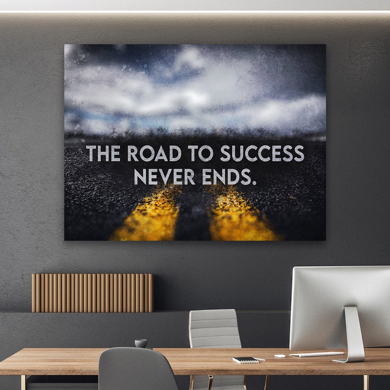K&ouml;nnte beinhalten: Leinwanddruck mit dem Text "THE ROAD TO SUCCESS NEVER ENDS." Das Bild zeigt eine Stra&szlig;e mit gelben Linien, die zu einem bew&ouml;lkten Himmel f&uuml;hrt. Das Kunstwerk wird an einer Wand &uuml;ber einem Holzschreibtisch pr&auml;sentiert.