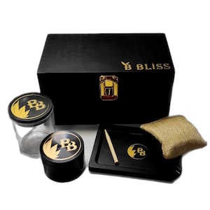 May include: Black wooden box with a gold latch and the text "B BLISS" on the top. The box contains a glass jar, a wooden grinder, a wooden rolling tray with a gold logo, a wooden poker, and a small burlap pouch.