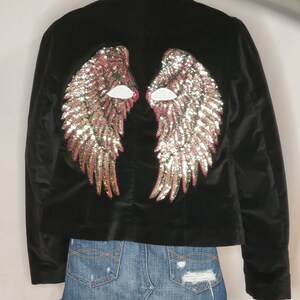 May include: Black velvet jacket with sequined angel wings on the back. The wings are pink, gold, and silver.