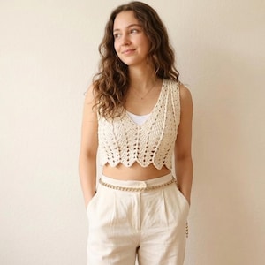 Peut inclure: Un haut court sans manches en crochet de couleur crème avec une encolure en V et un ourlet festonné, associé à un pantalon taille haute blanc cassé doté d'une ceinture à chaîne dorée à la taille, formant une tenue coordonnée aux tons clairs.