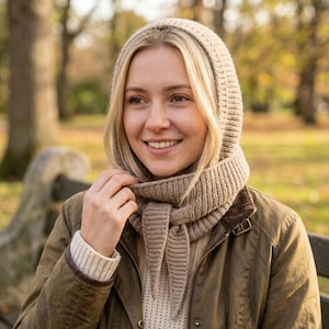 Può includere: Un passamontagna in maglia beige con una trama a coste che copre la testa e il collo, caratterizzato da due estremità appuntite che si annodano sul davanti. L'accessorio è realizzato in filato morbido e offre una copertura completa.