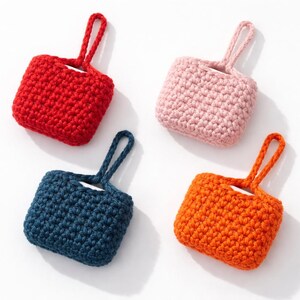 May include: Four small, crocheted cases in red, pink, navy blue, and orange. Each case has a small loop handle at the top. The cases are square-shaped and appear to be handmade, with a textured, knitted appearance.