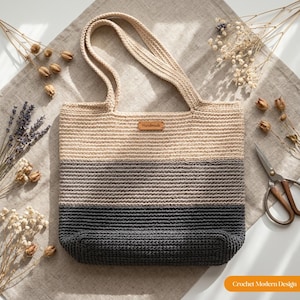 May include: A crochet tote bag featuring a horizontal color-blocked design in shades of beige, light gray, and dark charcoal gray. The bag has two matching beige handles and a small rectangular brown leather tag labeled Handmade centered at the top.