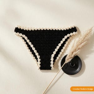 May include: Black crochet bikini bottom featuring a cream-coloured scalloped edge trim along the waistband and leg openings. The garment is displayed alongside a black ceramic dish and a dried pampas grass stem. Text reads Crochet Modern Design.