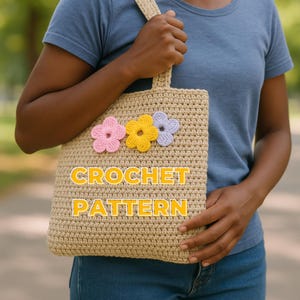 Peut inclure: Un sac fourre-tout en crochet beige orné de trois fleurs appliquées roses, jaunes et lavande. Le sac est de forme rectangulaire avec une anse et l'inscription "CROCHET PATTERN" en jaune.