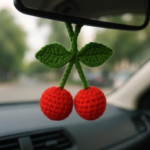 Peut inclure: Un porte-bonheur de voiture crocheté représentant deux cerises rouges vives avec des tiges et des feuilles vertes. Le charme est suspendu au rétroviseur d'une voiture, ajoutant une touche artisanale à l'intérieur du véhicule.