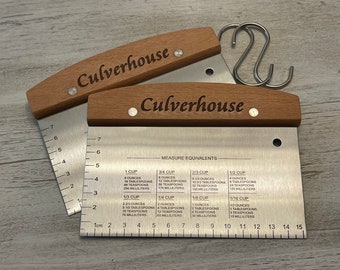 Peut inclure: Deux coupe-pâte en acier inoxydable avec des manches en bois. Les coupe-pâte sont gradués en centimètres et en tasses. Les manches sont gravés du texte "Culverhouse".