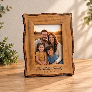 Puede incluir: Un marco de fotos rectangular de madera con un borde natural de corteza. El marco contiene una fotografía de una familia de cuatro personas y tiene grabado el texto The Miller Family EST. 2019 en la parte inferior central de la madera.
