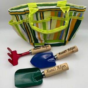 May include: A green, blue, and red gardening tool set with wooden handles. The handles are engraved with the words "Mama's Helper". The tools are in a striped green and yellow canvas bag.