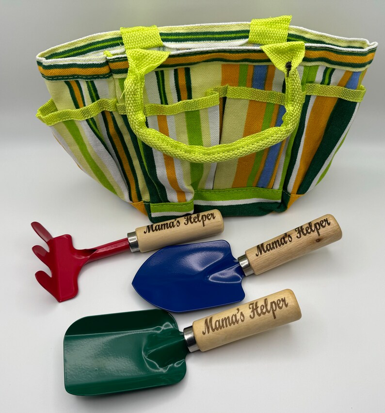 May include: A green, blue, and red gardening tool set with wooden handles. The handles are engraved with the words "Mama's Helper". The tools are in a striped green and yellow canvas bag.