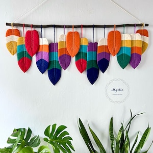 May include: A rainbow-coloured feather wall hanging with the word "Mystic" in a circle. The feathers are made of yarn and are arranged in a row.