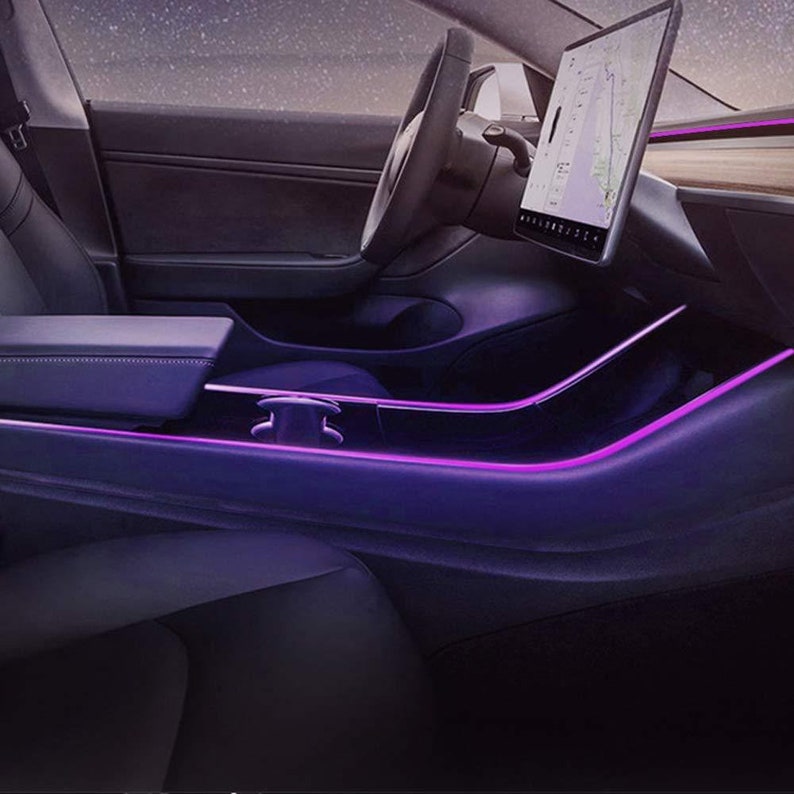 May include: The interior of a car with purple ambient lighting. The car has a black leather interior and a large touchscreen display.