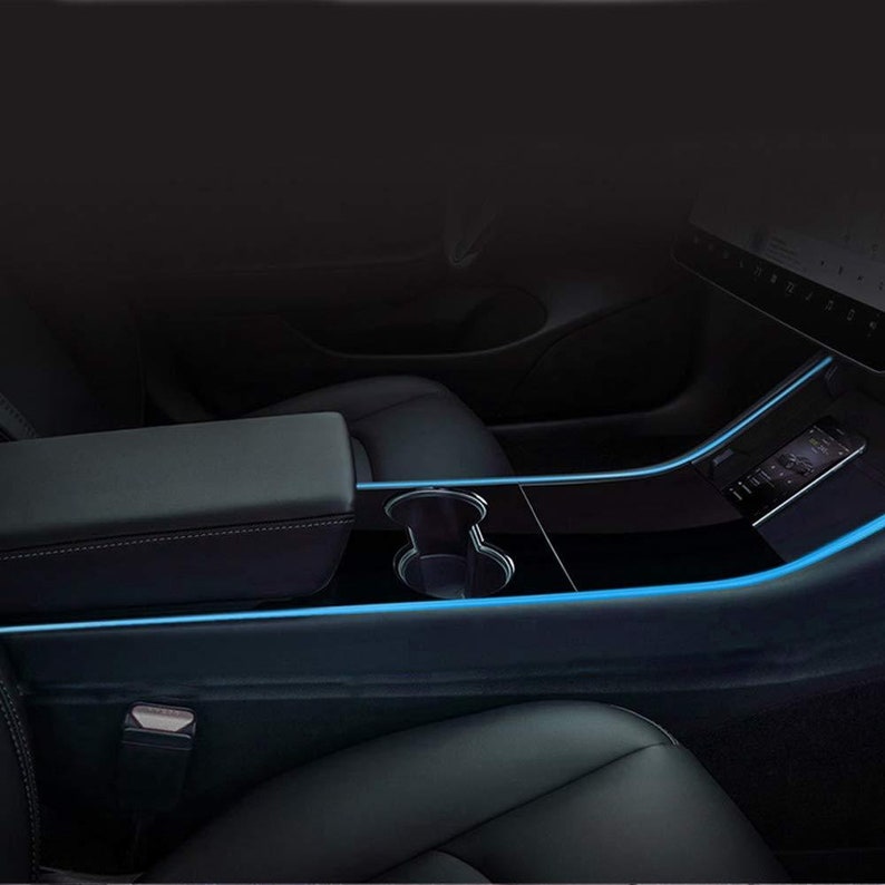 May include: A black leather car interior with a center console featuring a cupholder and a blue LED light strip along the edge.