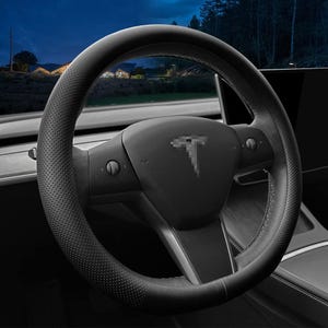 May include: Black leather steering wheel with a perforated design and a Tesla logo in the centre. The steering wheel is installed in a black car interior.