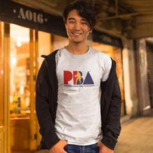 May include: A man wearing a white t-shirt with a blue, red, and yellow logo that says "PBA" and "Philippine Basketball Association". He is wearing a black jacket and blue jeans.