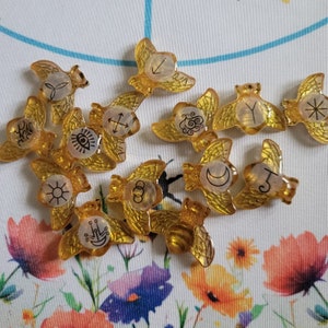 May include: A set of 12 gold-colored metal tokens with various symbols and designs. The tokens are shaped like wings and have a glossy finish.