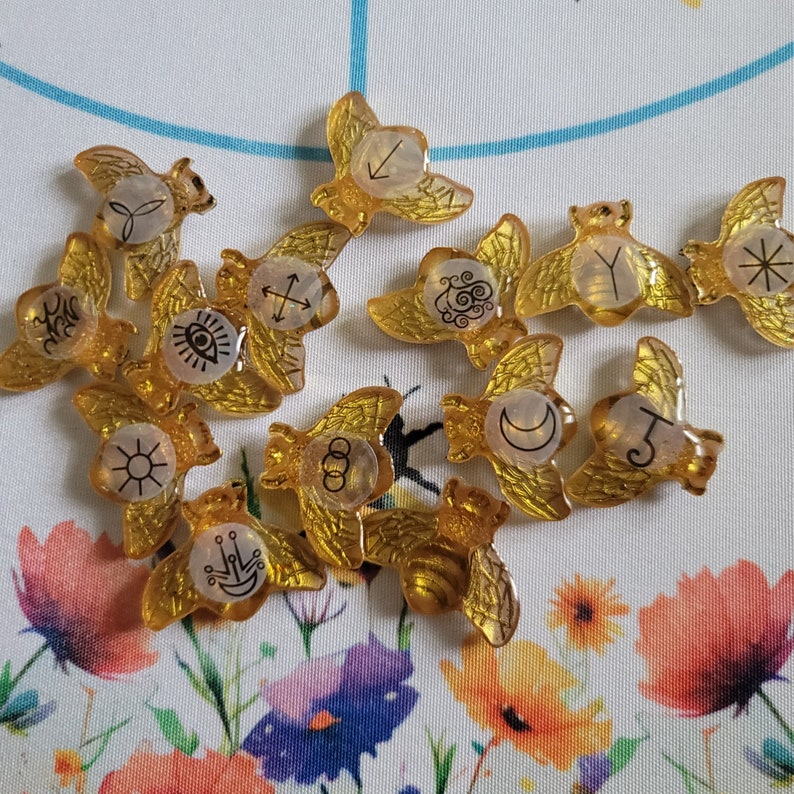 May include: A set of 12 gold-colored metal tokens with various symbols and designs. The tokens are shaped like wings and have a glossy finish.