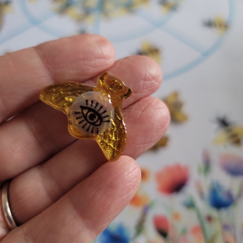 May include: A gold resin bee charm with a black eye design. The bee is translucent and has a glittery finish.
