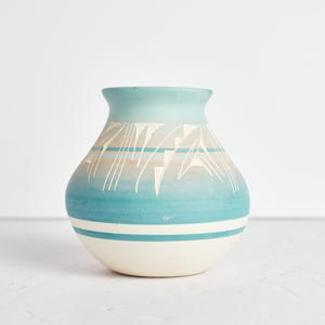 Peut inclure: Un petit vase en céramique blanche avec un motif géométrique bleu et blanc. Le vase a un corps arrondi et une large ouverture.